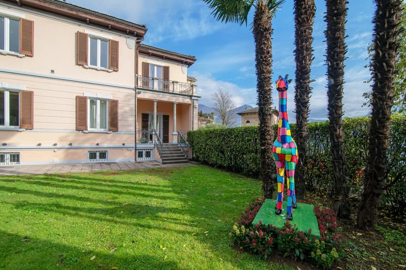 two story house with pink exterior, wooden doors, green lawn, colorful statue