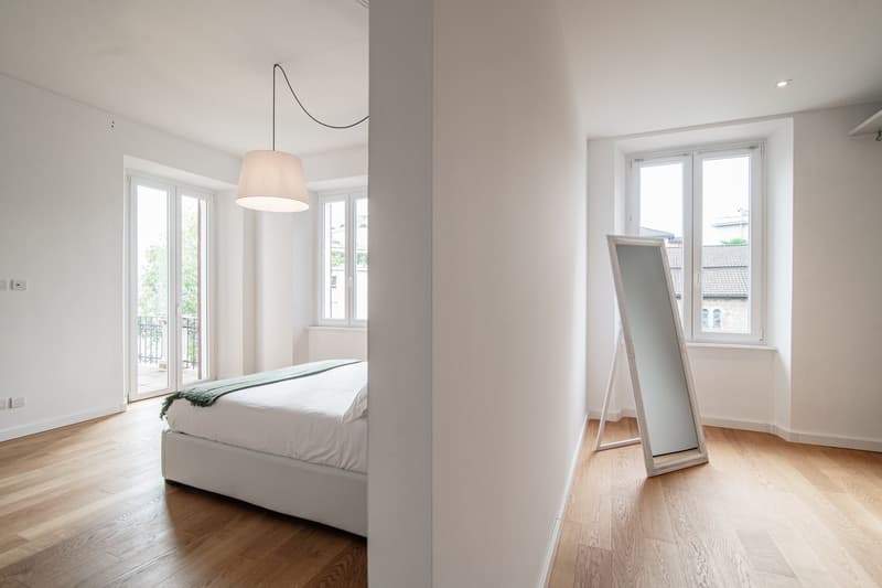 modern bedroom with bed, windows, sliding balcony doors, white ceiling, floor, and walls, simple decor