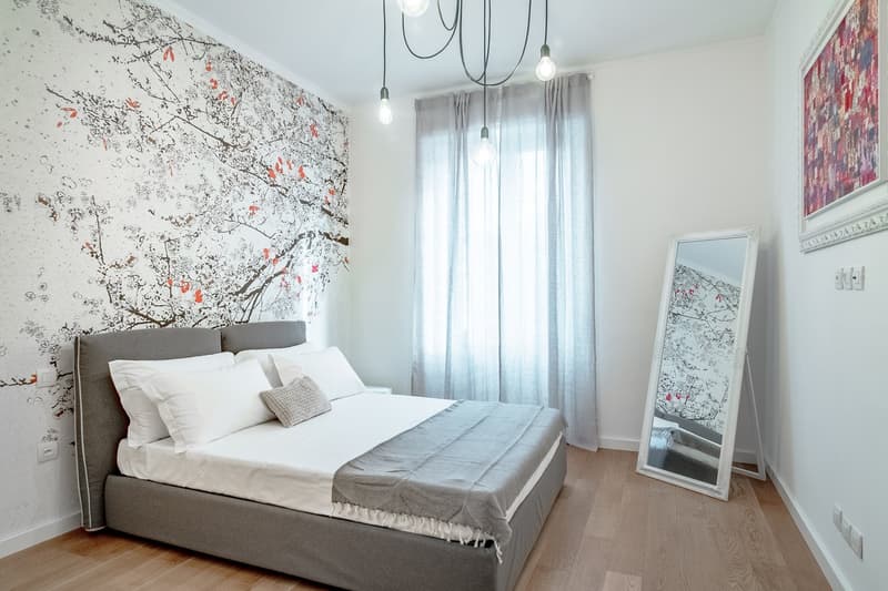 Modern bedroom with bed, wall art, mirror, lamps, wooden floor, and white linens