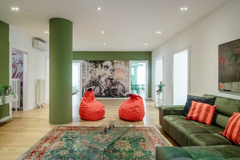 green couch, two orange bean bag chairs, rug, mural, radiator, central column