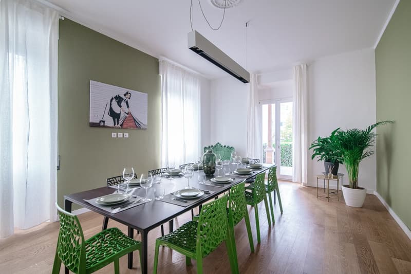 Green chairs, long table, wine glasses, plates, plants, picture on the wall, curtains