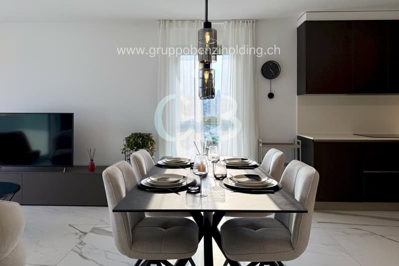 Dining room with dining table, chairs, TV, cabinet, and chandelier. There is also a plant and clock.