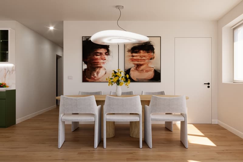 Spacious dining area with a wooden dining table and three gray upholstered chairs. The room features a large modern light fixture and artwork on the walls. There is a white door visible in the background.