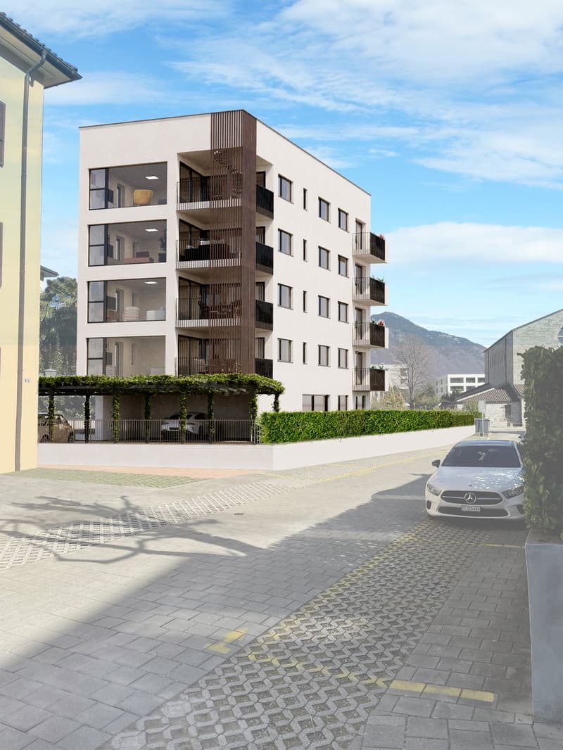 5-story apartment building with white exterior, wooden balcony railings, and landscaping around the building. There is a paved walkway and a parked car in the foreground.