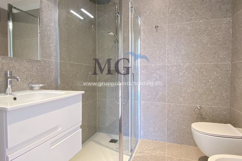 Modern bathroom with glass shower, white ceramic tiles, white vanity, silver faucet, silver shower head, mirror, and toilet