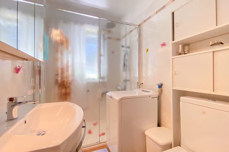 White bathroom with sink, shower cubicle, washing machine, and toilet