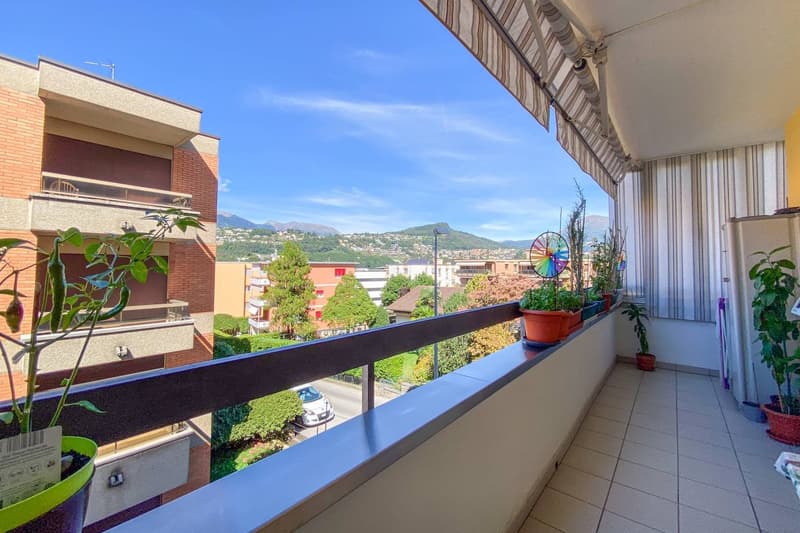 Balcony with tile flooring, black railing, multiple potted plants, awning, scenic view of mountains
