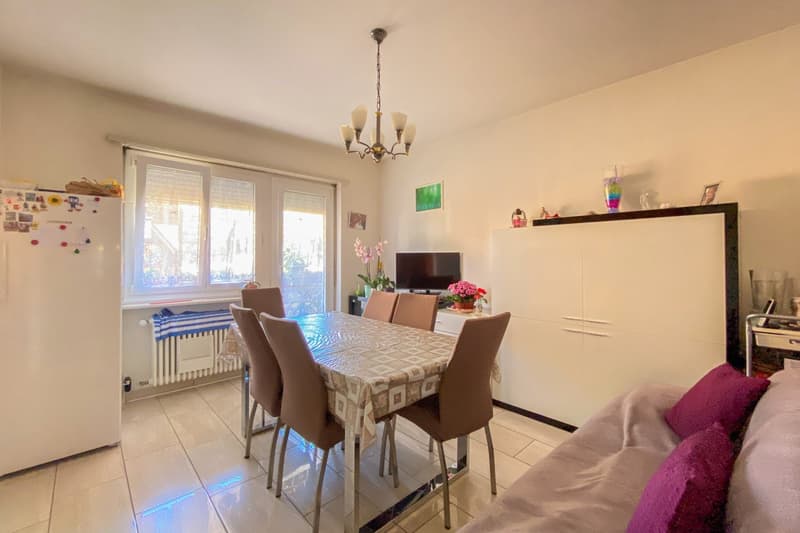 6 chairs around table, TV on shelf, white refrigerator, white floor, chandelier on ceiling