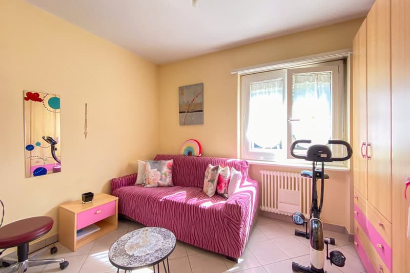 Living room with a pink sofa, wooden table, white tiled floor, pink cabinet, and window with curtains