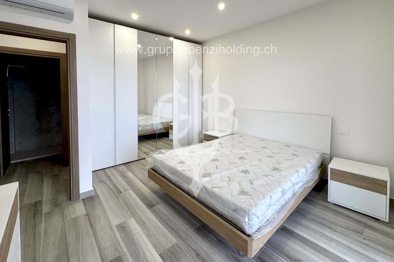 Bedroom with bed, nightstands, sliding wardrobe, air conditioning, hardwood floors, and a glimpse of a bathroom.