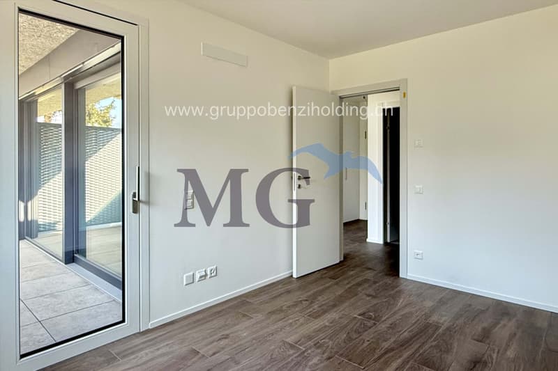 Sliding doors leading to a balcony, large glass window, wooden floor, white walls, power outlets, open door