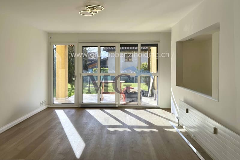 Modern room with sliding glass doors leading to a balcony, wooden floor, neutral colored walls, contemporary ceiling light.