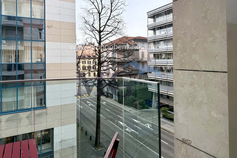 large windows, glass railings, red chair, outside tree, buildings, road, cars