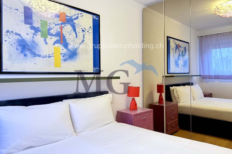 Main bed, side tables with lamps, mirrors, second bed in background