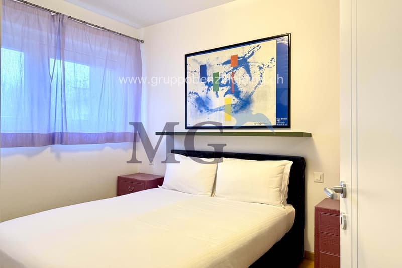 Bedroom with a bed, two nightstands, artwork on the wall, white curtains, wooden floor