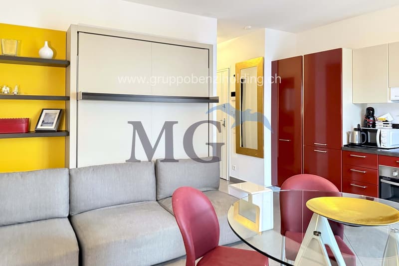Modern living area with couch, glass table, dining chairs, red kitchen cabinets, yellow accent wall