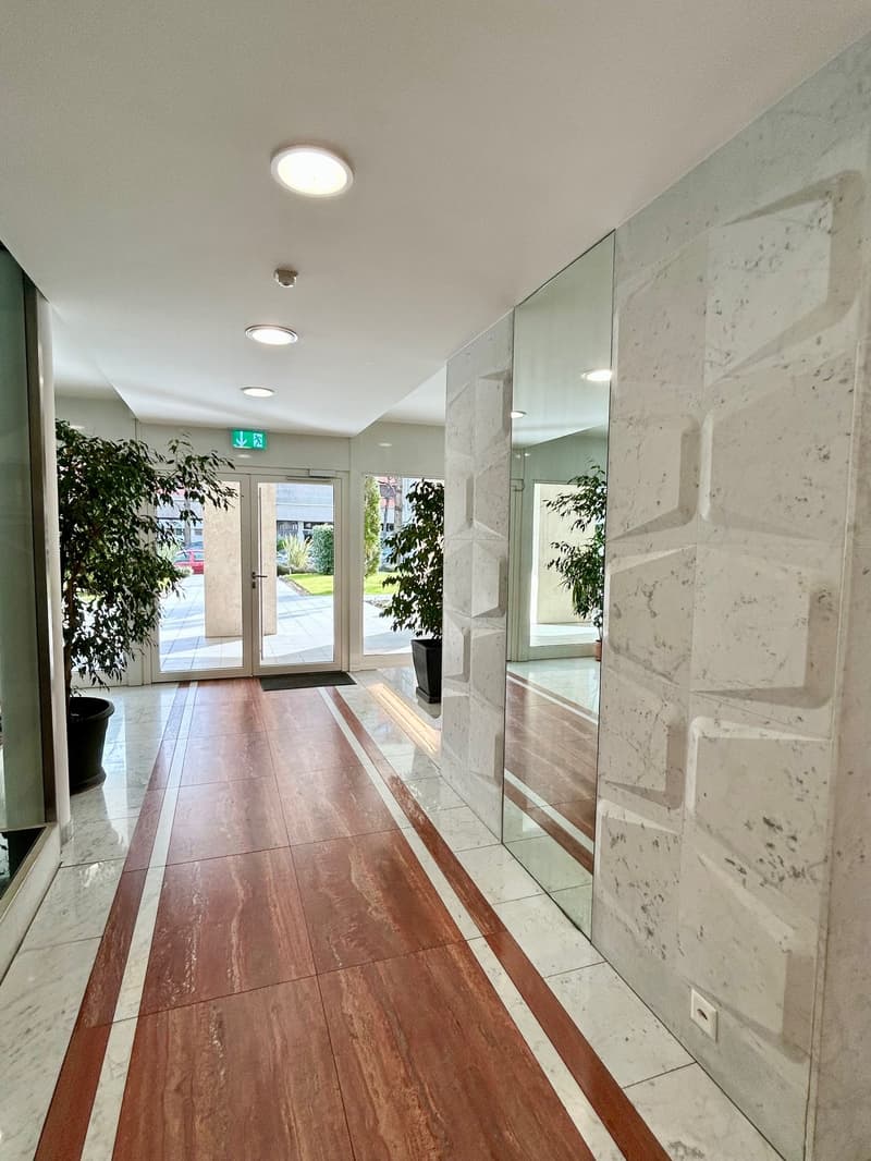 Marble floor, wooden floor, large mirror, plants, exit sign, ceiling lights