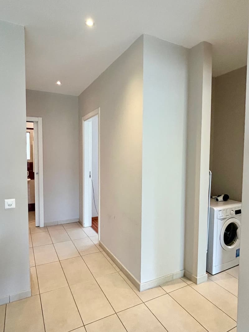 Empty room with white walls, tiled floor, and a washing machine in a corner