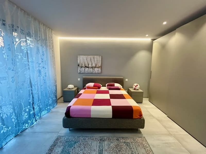 Bedroom with bed, two nightstands, white floral print pillow, bedspread, and a painting on the wall.