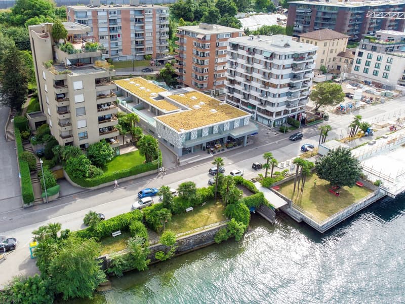 Multi-story apartment buildings with balconies, green landscaping, and a waterfront location with parking spaces
