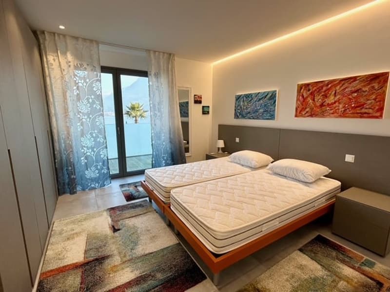 Bedroom with two single beds, two lamps, carpet, two nightstands, large glass door with balcony, curtains, artwork on the wall.