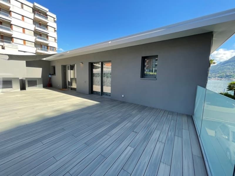 Modern apartment with a large balcony or terrace, gray exterior walls, and sliding glass doors leading to the outdoor space.
