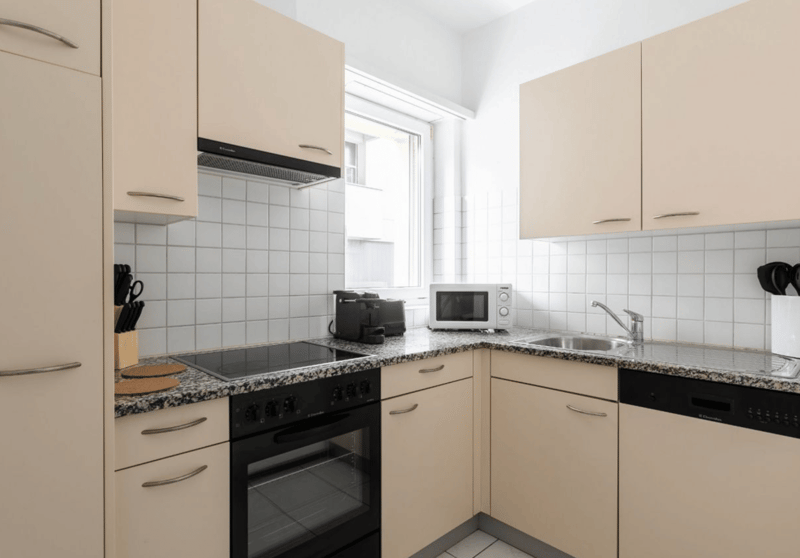 modern kitchen with white tiles, granite countertop, black oven, microwave, sink, dishwasher, toaster, knives, and utensils