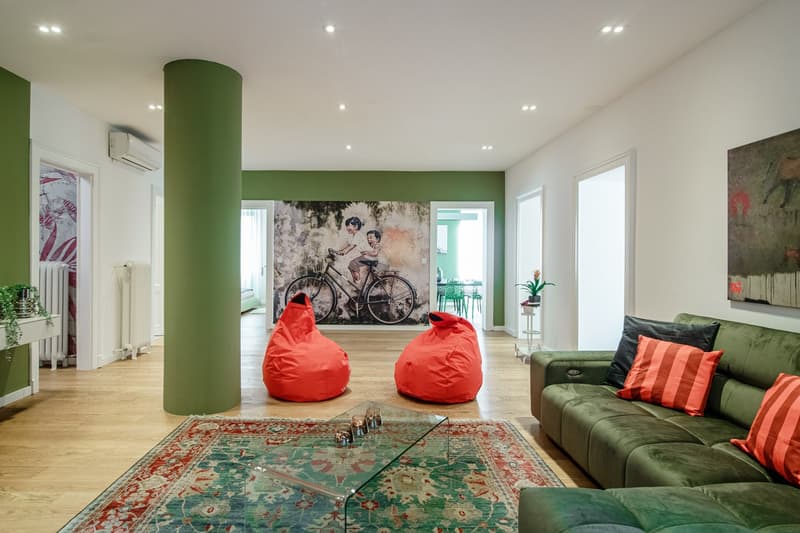 Green walls, wooden floor, modern style, green couch, red bean bags, coffee table, decorative rug, art pieces