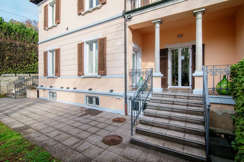 Two story house, pink wall, grey tiles, wooden windows, white shutters, metal railings, two steps leading up to the door