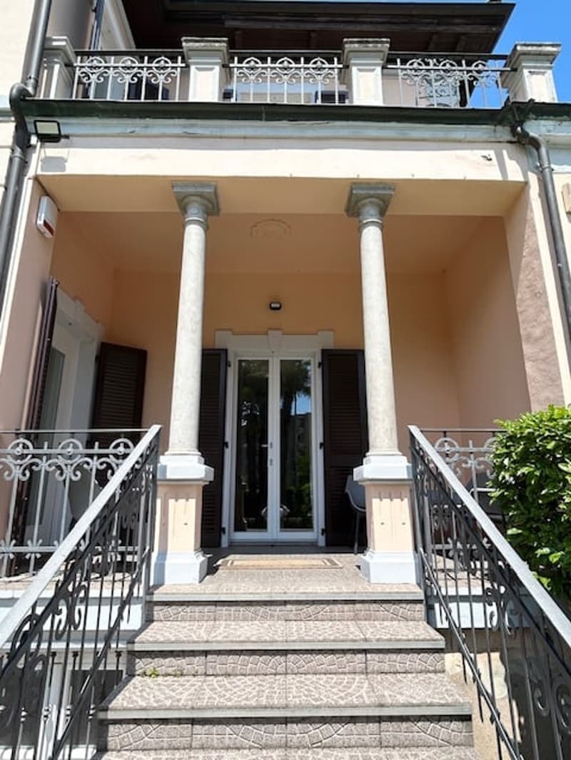 Two-story building with a balcony on the upper level, ornate railings, and columns supporting the entrance porch.