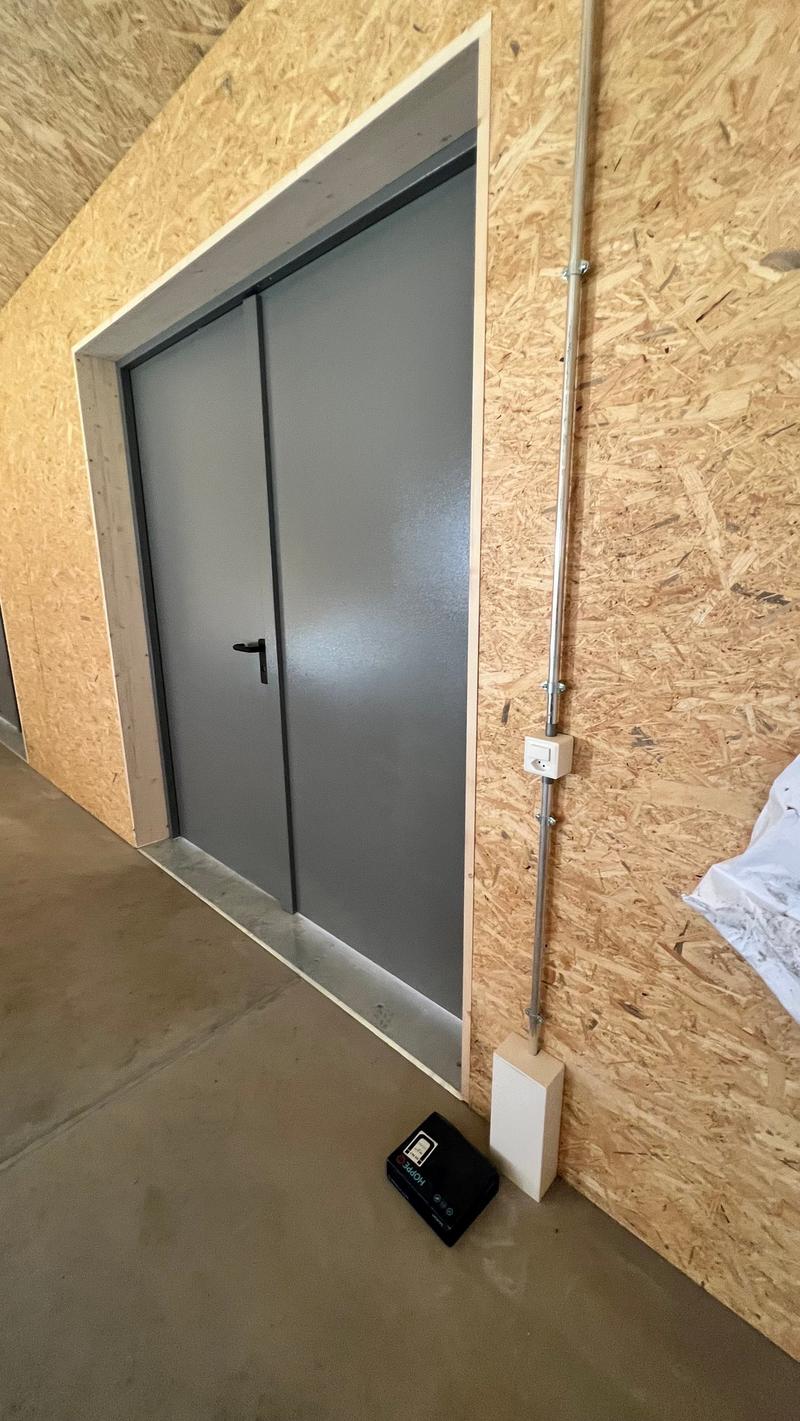 A gray metal sliding door with a white frame, installed in an OSB (oriented strand board) wall.
