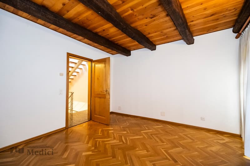 Empty room, wooden floor, white walls, wooden ceiling, door, staircase visible