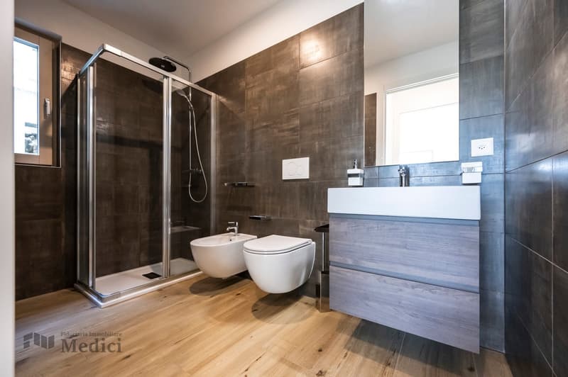 Modern bathroom with walk-in shower, two toilets, and vanity unit with sink.