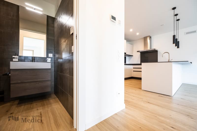 Modern bathroom with white and gray tiled walls, wooden floor, large mirror, white sink, dark faucet, white cabinet