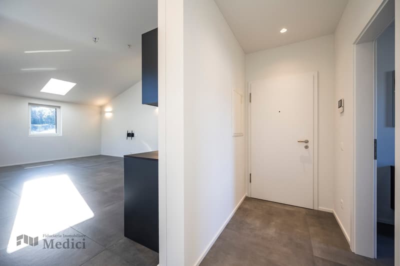 Empty room, grey flooring, white walls, a small counter on the left, a skylight on the ceiling