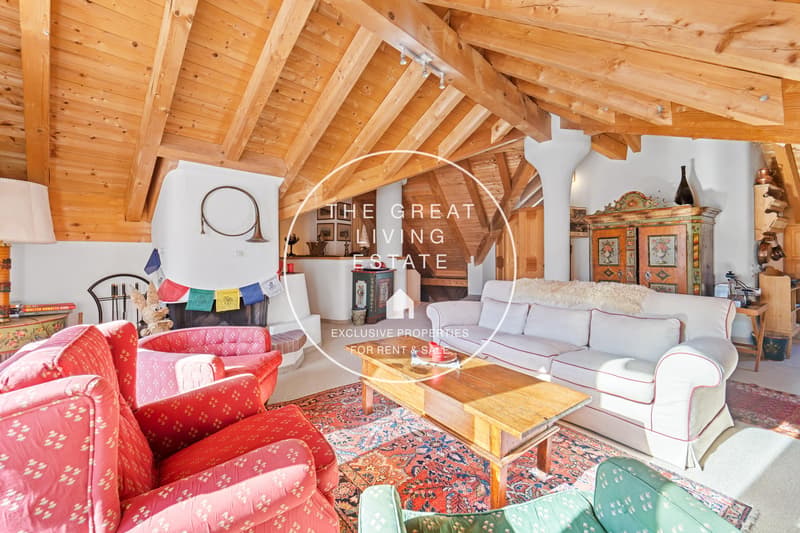 Spacious living room with wooden beamed ceiling, colorful patterned sofas and armchairs, wooden coffee table, and a fireplace. The room has a cozy and eclectic decor style.