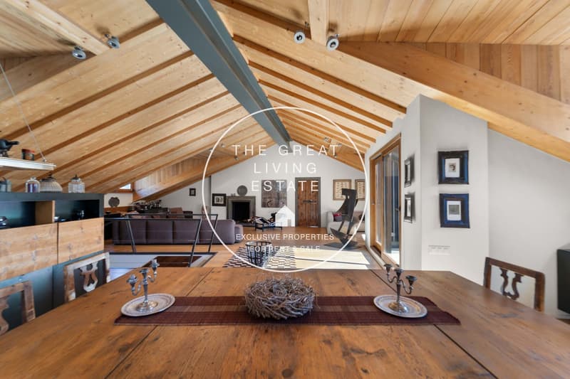 large dining room, wood beams ceiling, dining table with chairs, wooden floor, lamps, open to living room with couch and fireplace