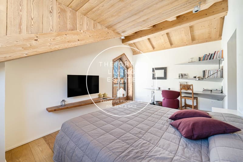 Wooden floor, White walls, large bed, TV, wooden desk, shelves with books, chair, wooden ceiling