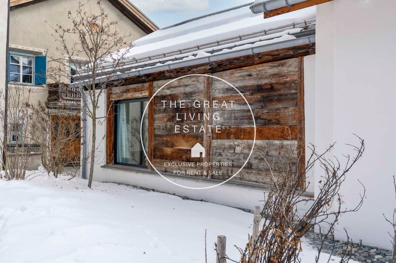 Wooden and brick house exterior, snowy roof, two windows, snow-covered ground