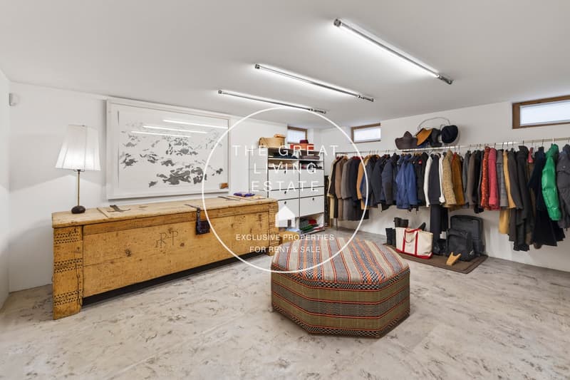 Clothing closet with clothes, hats, and bags, wooden trunk with lamp, ottoman