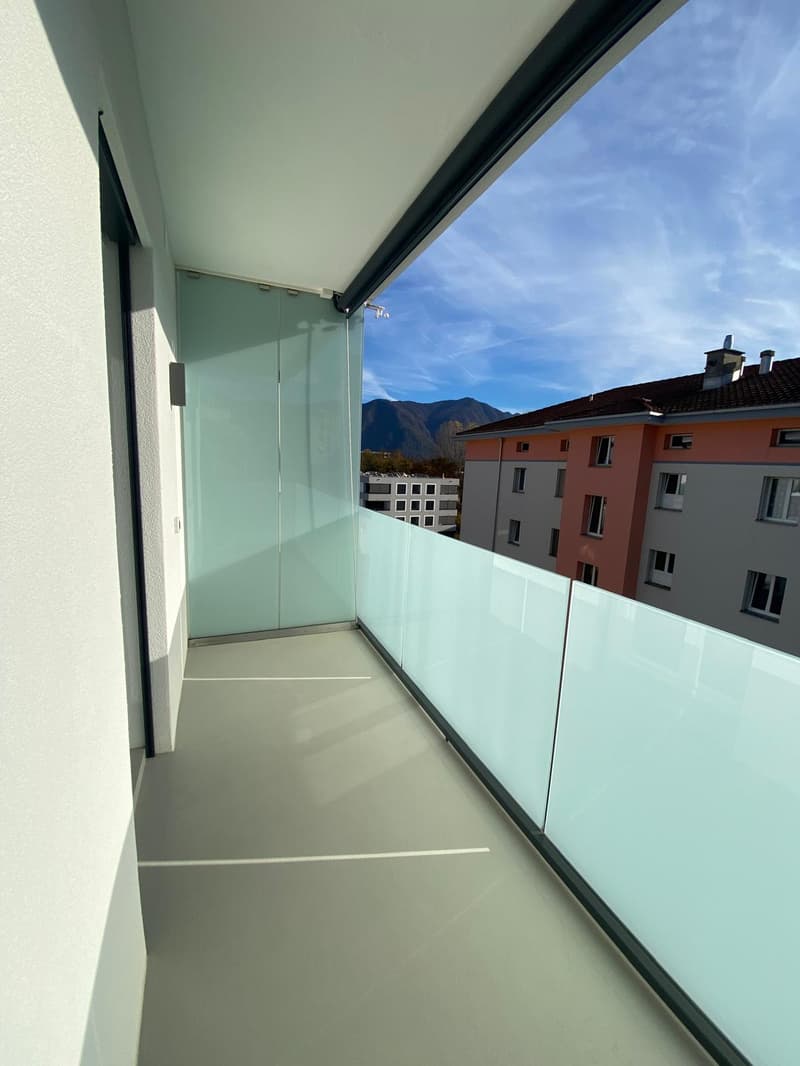 Empty balcony with large glass balustrade, white walls, large white glass doors, view of buildings, mountains