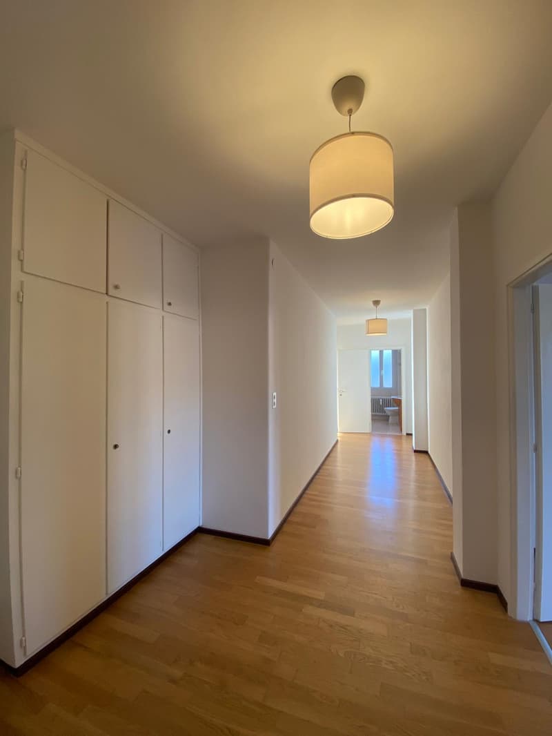 an empty corridor with white cabinets and wooden floors