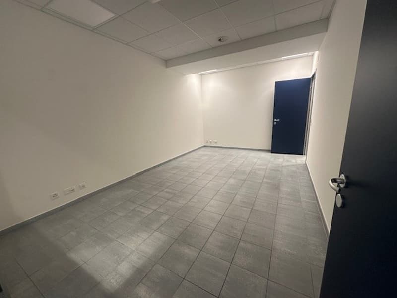 An empty room with white walls, a blue door, tiled flooring, and several power outlets on the walls.