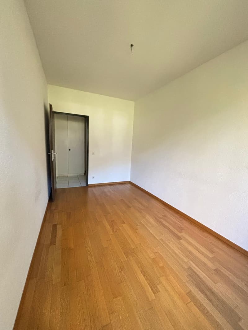 large room, wooden floors, white walls, open door to hallway, no furniture