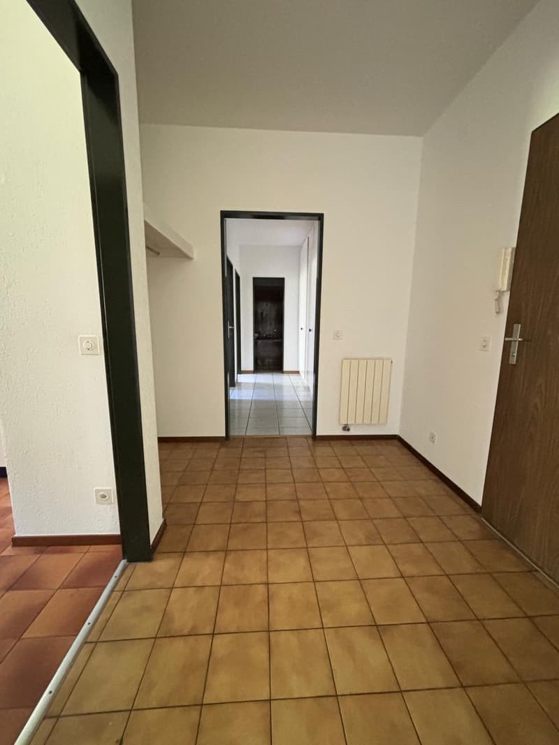 empty room with tile flooring, white walls, wooden door, radiator, 3 power outlets