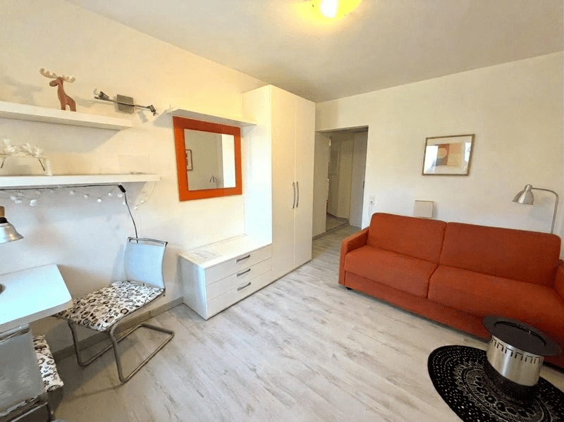 A small living room with a couch, a desk, a chair, a mirror, and a lamp.