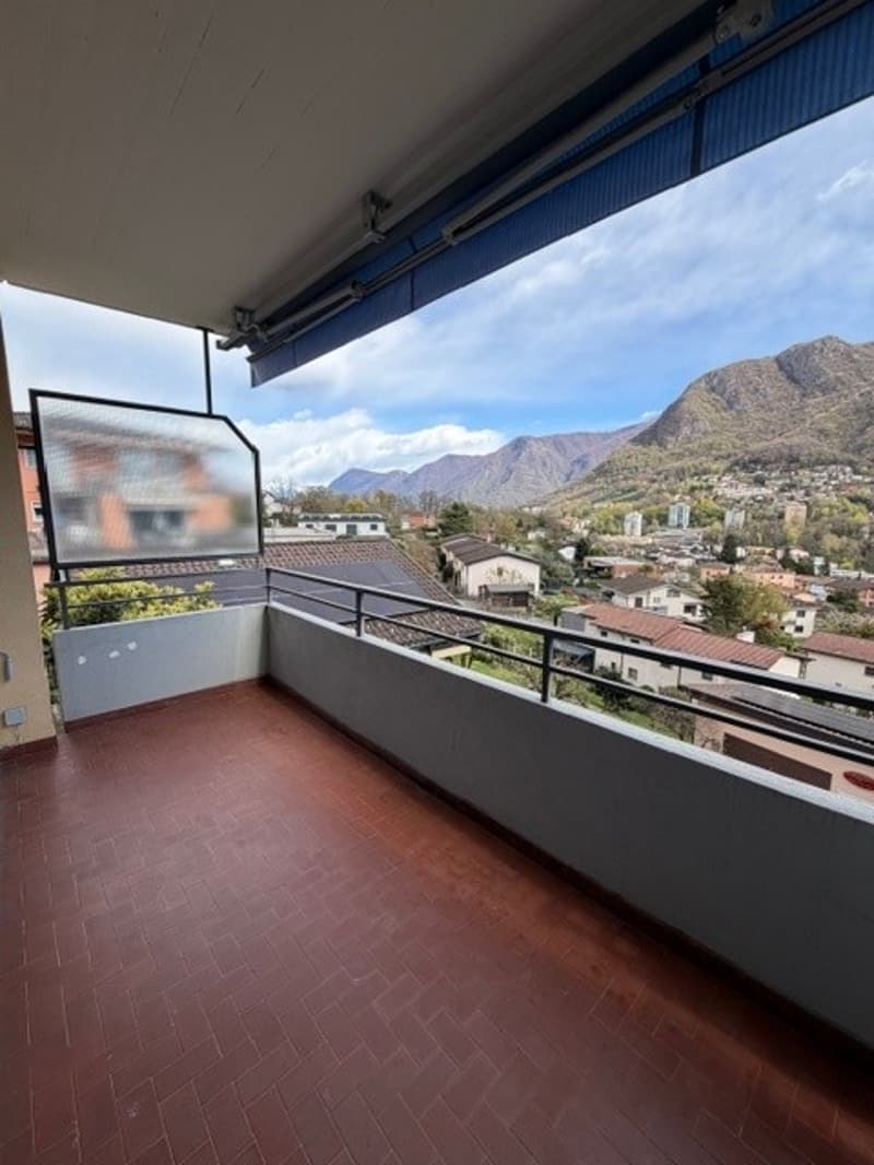 Balcony with red tile floor, metal railing, glass wall, view of mountains and town
