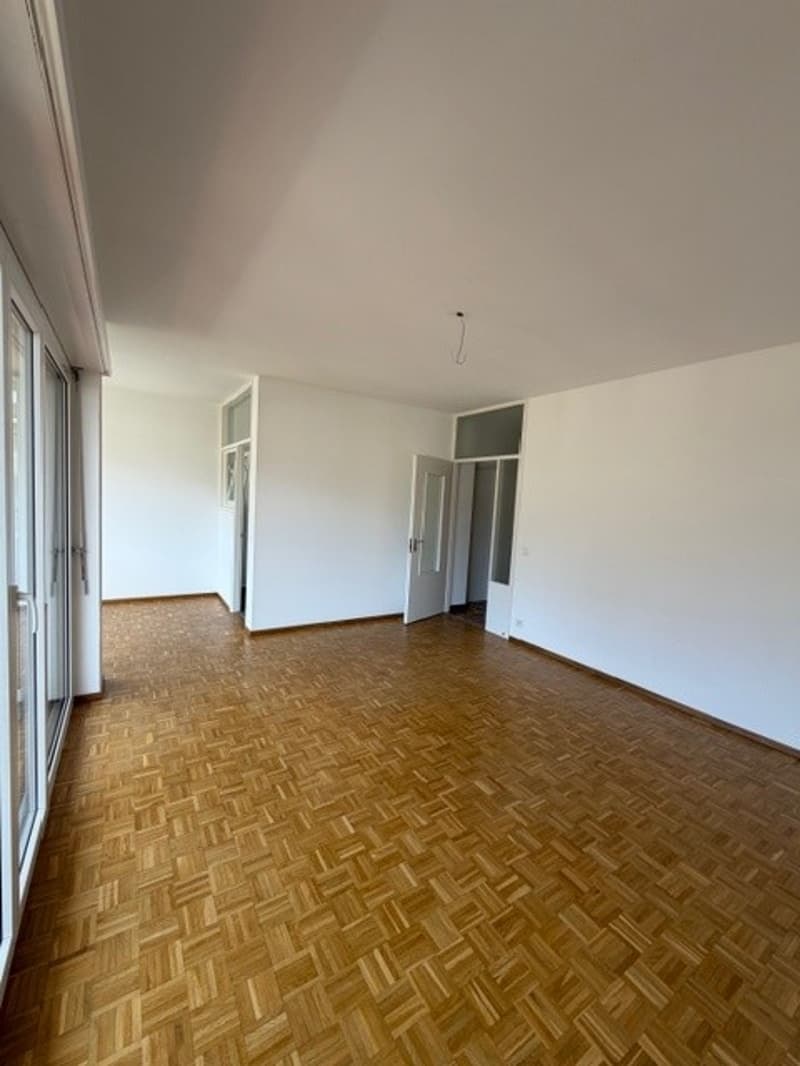 Empty room with wooden floor, white walls, glass doors, and an open door.