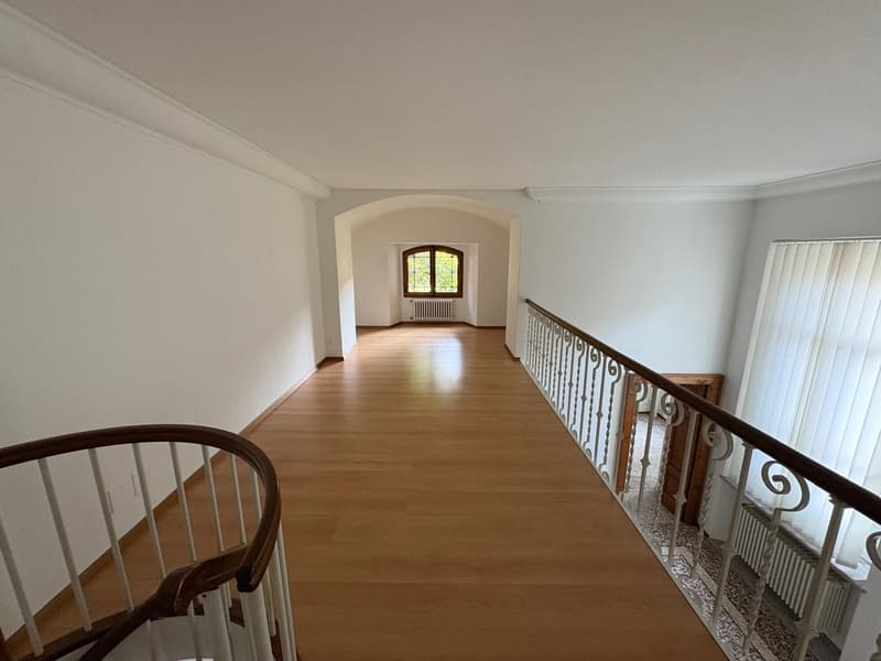 wide hallway, wooden floor, spiral staircase, white walls, arched doorway