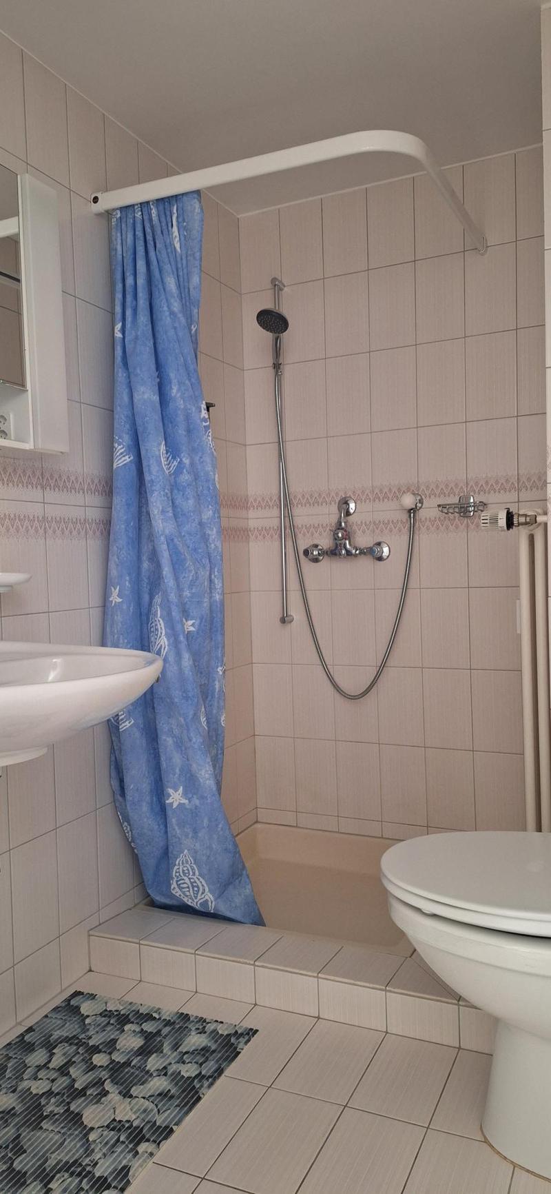 A small, clean, and modern bathroom with white tiled floor and walls, featuring a shower area with a shower curtain, a toilet, a sink with a mirror, and a showerhead.